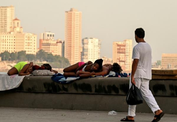 Un homme passe devant des femmes qui dorment sur le Malecon à La Havane lors d'une coupure de courant nationale, le 3 août 2026