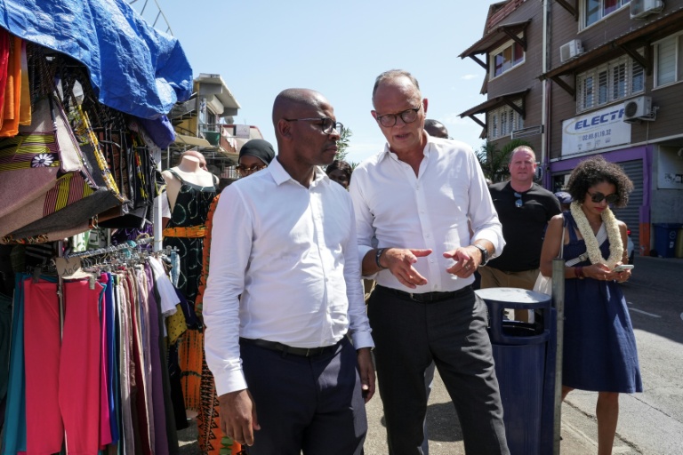 Édouard Philippe (c), fondateur et président du parti Horizons, maire du Havre et candidat à l'élection présidentielle, et Ambdilwahedou Soumaila (g), maire de Mamoudzou visitent une rue commerçante de Mamoudzou, le 21 août 2026 sur l'île de Mayottte