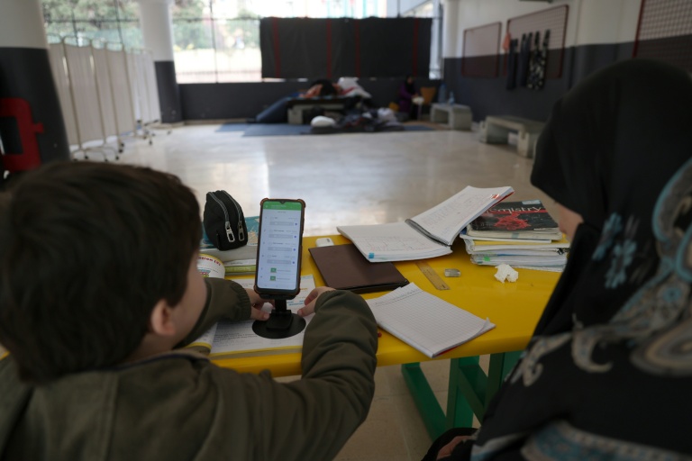 Une femme, assise à côté d'un enfant, supervise ses études en ligne sur un téléphone portable dans une école publique transformée en refuge pour personnes déplacées, à Dekwaneh, au nord de Beyrouth, le 25 mars 2026 au Liban