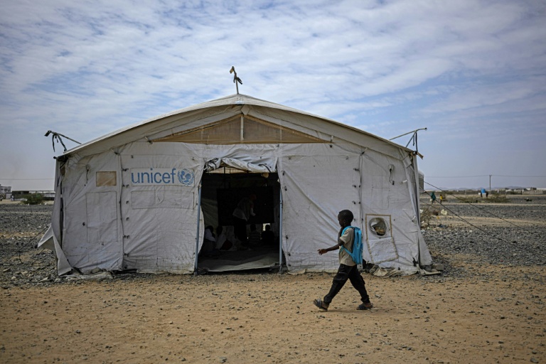 Un élève passe devant une tente servant d'école dans un camp de personnes déplacées par la guerre, près de Port-Soudan, le 26 avril 2026 au Soudan
