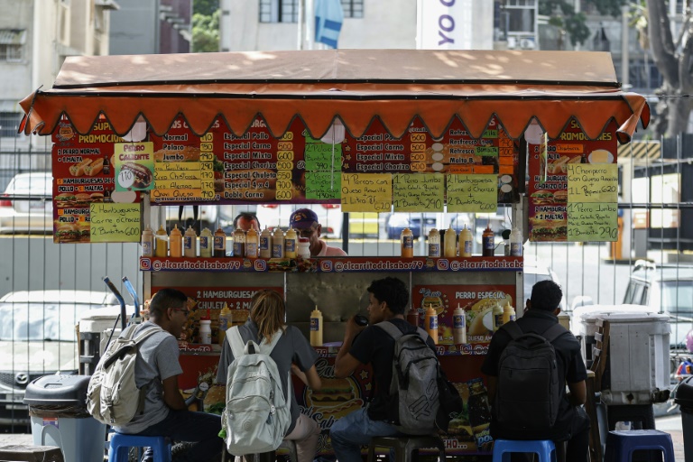 Des clients mangent à une échoppe de rue où les prix sont affichés en bolivars (monnaie officielle vénézuélienne) à Caracas, Venezuela, le 2 juin 2025