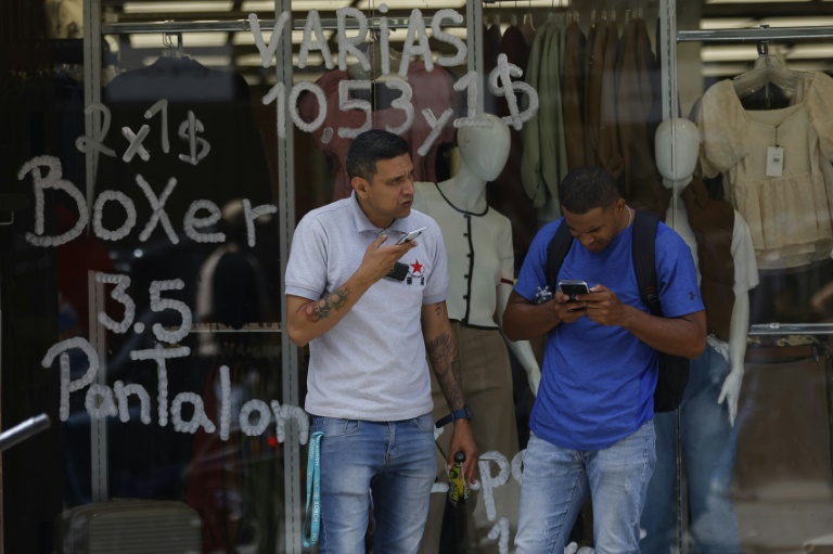 Des habitants devant un magasin affichant les prix en bolivars (monnaie officielle vénézuélienne) et en dollars américains à Caracas, au Venezuela, le 2 juin 2025