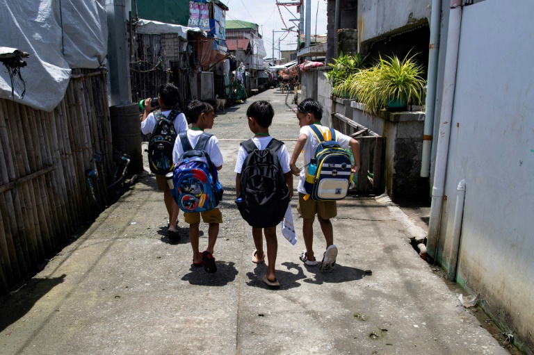 Des enfants sur un trottoir sec, en chemin pour l'école, sur l'île de Pugad, dans la province de Bulacan, le 7 juillet 2025 aux Philippines