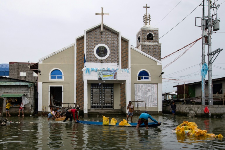 Des ouvriers déchargent des sacs de sable sur un chantier de construction devant une église dans une rue inondée de l'île de Pugad, dans la province de Bulacan, le 21 août 2025 aux Philippines