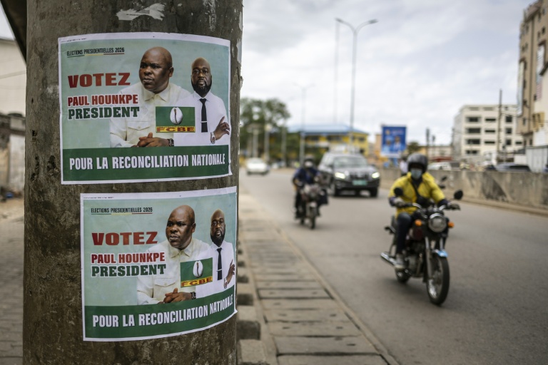 Des habitants de la capitale béninoise circulent à moto et en voiture près d'une affiche électorale, le 9 avril 2026 à Cotonou