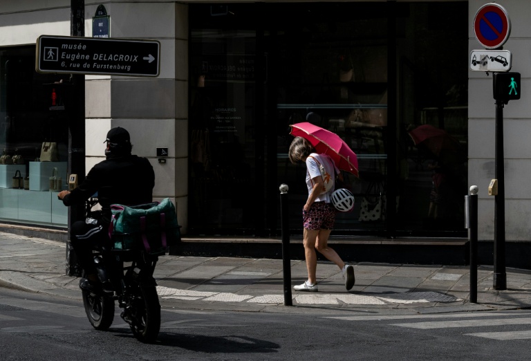 Une passante se protège du soleil avec un parapluie dans une rue à Paris, le 13 juillet 2026 lors d'un épisode de canicule en France