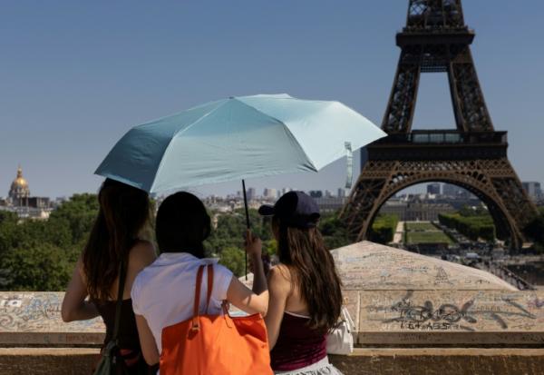 Des touristes se protègent du soleil sous un paraplluie devant la Tour Eiffel lors d'une vague de chaleur à Paris, le 27 mai 2026