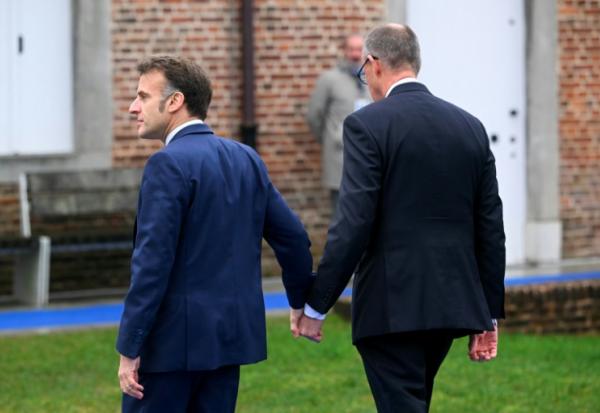 Emmanuel Macron (G) et Friedrich Merz se tiennent la main à leur arrivée au sommet informel de l'UE au château belge d'Alden Biesen en Belgique le 12 février 2026
