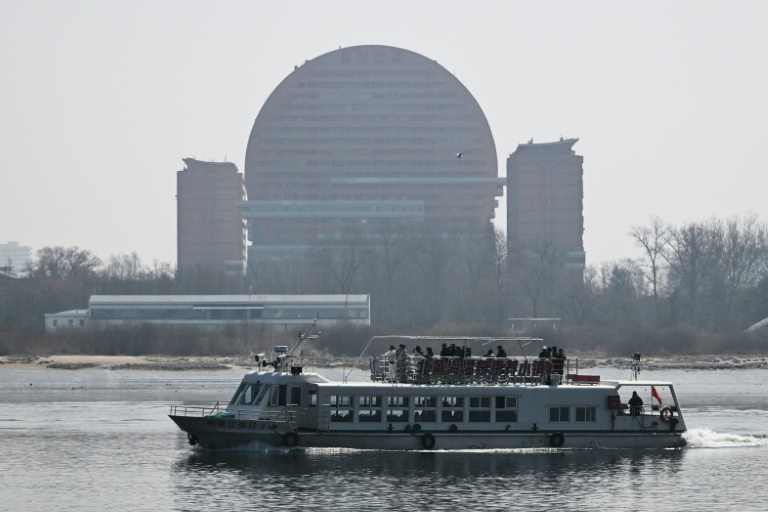 Un bateau touristique chinois sur le fleuve Yalu passe devant un hôtel de la ville nord-coréenne de Sinuiju, face à la ville frontalière de Dandong, dans le nord-est de la Chine, le 26 mars 2026