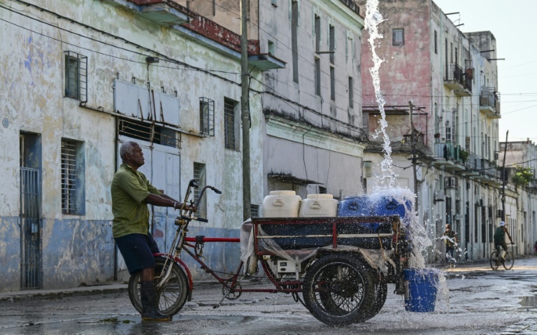 Un homme remplit des récipients d'eau à un point de ravitaillement public dans une rue de La Havane, le 5 octobre 2026
