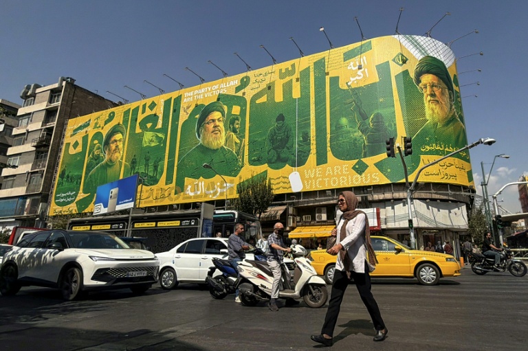 Des piétons et des automobilistes passent devant un panneau d'affichage géant représentant le chef assassiné du Hezbollah libanais, Hassan Nasrallah (G), et le guide suprême défunt iranien, l'ayatollah Ali Khamenei (D), le 27 septembre 2026 à Téhéran