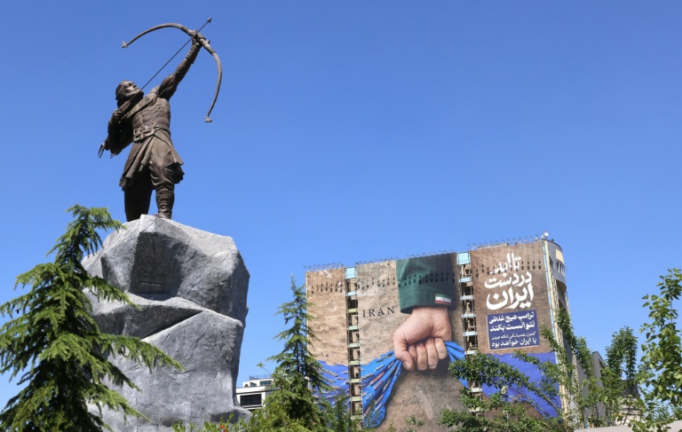 Une sculpture moderne d'Arash l'Archer, figure légendaire de la mythologie persane, devant affiche géante sur la façade d'un immeuble représentant le détroit d'Ormuz avec l'inscription en persan 