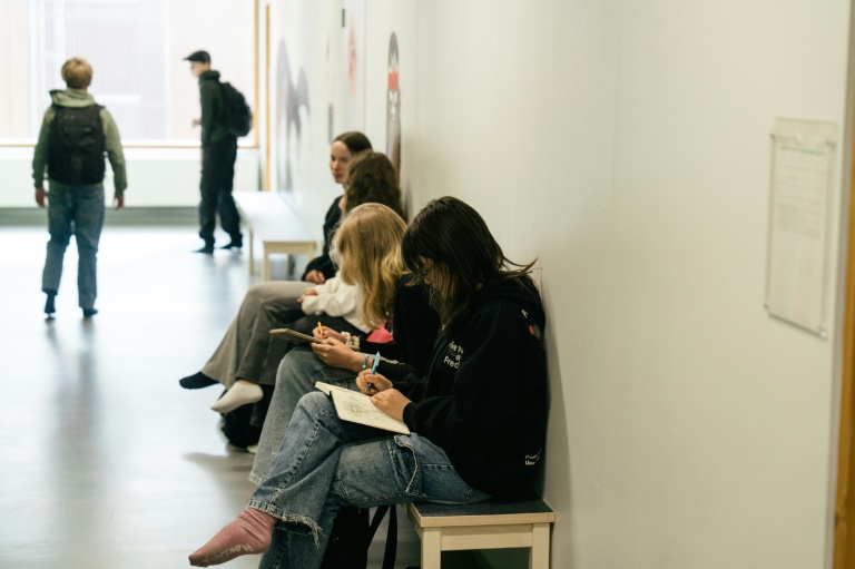 Des élèves assis sur un banc dans un couloir pendant une pause entre les cours au  collège Kungsvägens skola, le 21 août 2025 à Sipoo, en Finlande