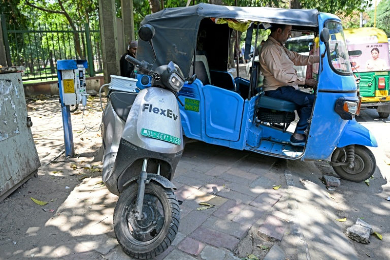Un conducteur de rickshaw recharge son véhicule à côté d'un scooter électrique, à New Delhi, en Inde, le 12 avril 2026
