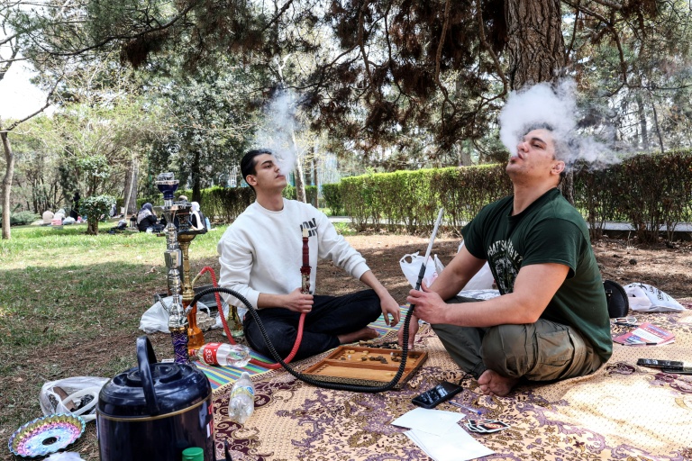 Deux Iraniens fument la chicha assis dans le parc Mellat de Téhéran, le 2 avril 2026, lors de la 