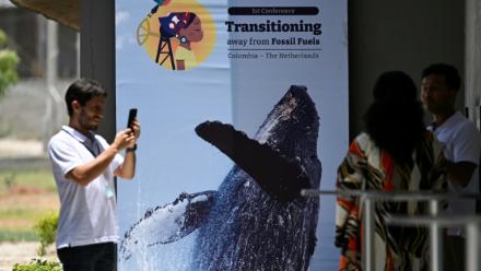 Des personnes prennent une photo devant une affiche de la conférence pour une sortie des énergies fossiles, à Santa Marta, en Colombie, le 26 avril 2026