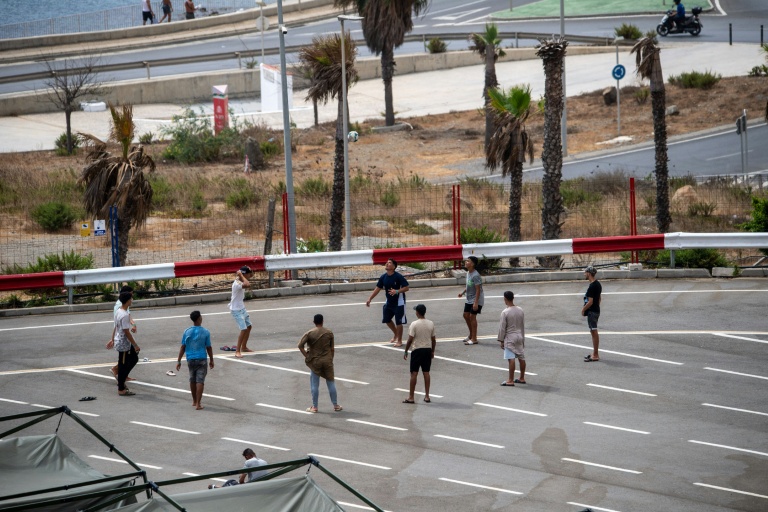 Des migrants jouent au foot sur un parking près d'abris temporaires installés pour eux, le 27 août 2026 à Ceuta