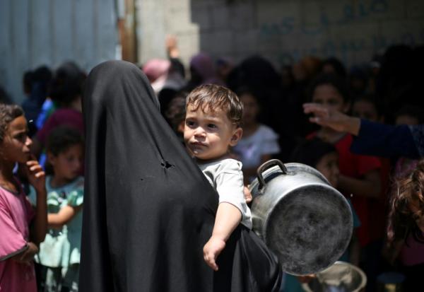 Une Palestinienne portant un enfant dans une file d'attente à un distribution de repas chauds à Nousseirat, dans le centre de la bande de Gaza, le 4 juin 2025