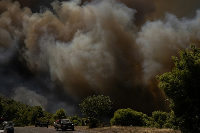 Des véhicules de secours stationnés au premier plan tandis que de la fumée s’élève d’un incendie de forêt à l’arrière-plan, dans la région de Porto Germeno, le 1er août 2026