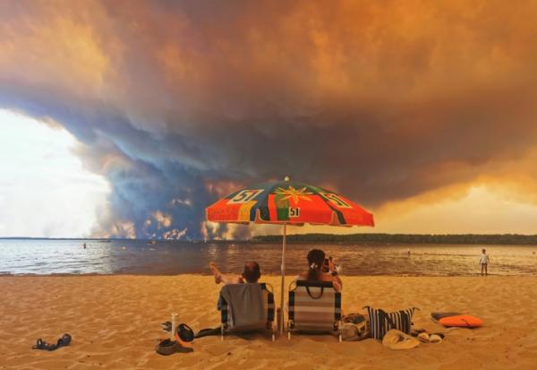 Des personnes sur la plage du Moutchic à Lacanau, dans le sud-ouest de la France, le 24 juillet 2026, tandis que des nuages de fumée d'un incendie s’élèvent dans le ciel 