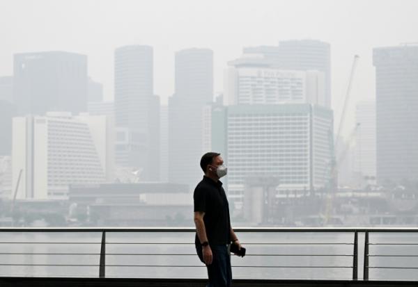 Un passant porte un masque de protection le long du boulevard à Marina Bay, noyé dans la brume, le 12 octobre 2026 à Singapour 