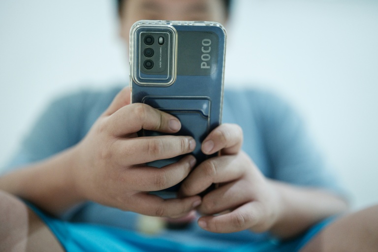 Bradley Rowen Liu, 11 ans, regarde une vidéo sur son téléphone le 25 mars 2026 à Jakarta, en Indonésie