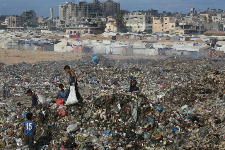 Des enfants palestiniens cherchent des objets à sauver dans un tas d'ordures près de destructions dans le camp de réfugiés de Bureij, dans le centre de la bande de Gaza, le 6 octobre 2025