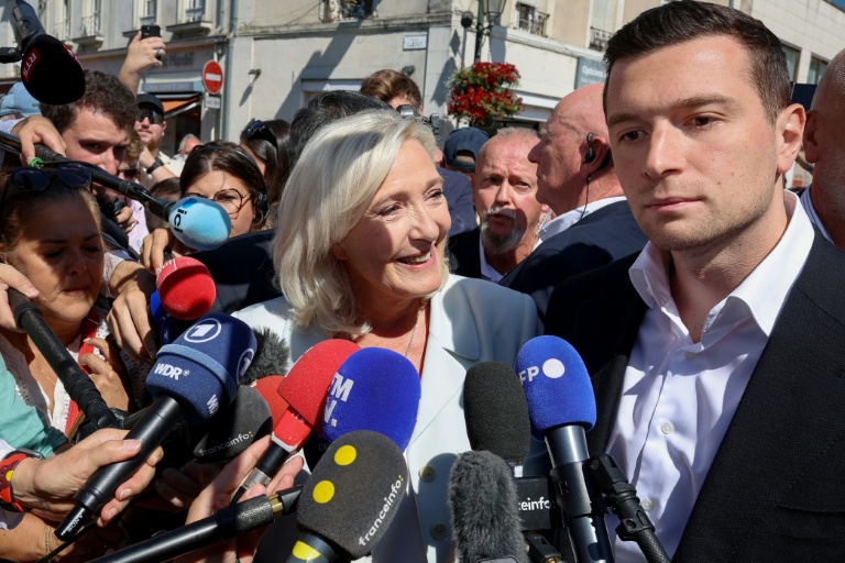 Marine Le Pen (c), cheffe du groupe parlementaire Rassemblement national (RN) et candidate à la présidentielle de 2027, et Jordan Bardella, président du RN, entourés de journalistes à leur arrivée à La Flèche pour un rassemblement de campagne, le 8 juillet 2026 dans la Sarthe