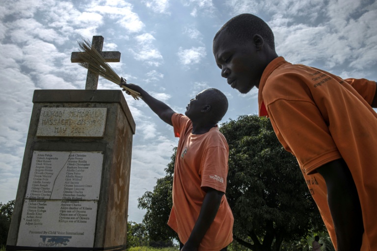 Wilfred Lalobo (centre), 60 ans, un survivant du massacre de Lukodi le 19 mai 2004, et Richard Ochola, 34 ans, un employé du mémorial de Lukodi, nettoient une stèle commémorative du massacre perpétré il a plus de 20 ans par la guérilla de la LRA dans ce village du nord de l'Ouganda, le 4 septembre 2025