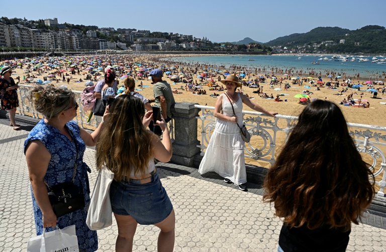 Des touristes prennent des photos sur l'esplanade longeant la plage de la baie de La Concha, dans la ville basque espagnole de Saint-Sébastien, le 10 août 2025