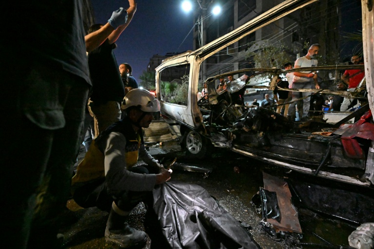 Des passants et des secouristes inspectent la carcasse du minibus dans lequel une bombe a explosé, à Jaramana, près de la capitale syrienne, Damas, le 6 août 2026