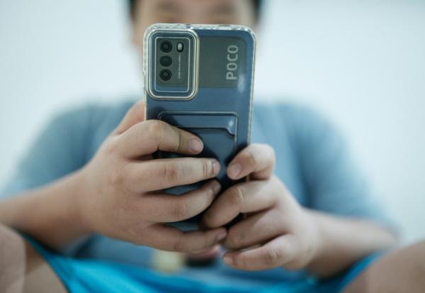 Un petit garçon regarde une vidéo sur son smartphone en attendant son père, à Jakarta, le 25 mars 2026