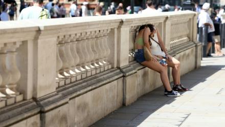 Des personnes se protégent du soleil derrière un mur, le 24 juin 2026 à Londres