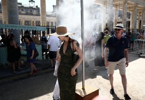 Des piétons se rafraîchissent sous un brumisateur installé par la mairie de Paris pendant une vague de chaleur à Paris, le 21 juin 2026