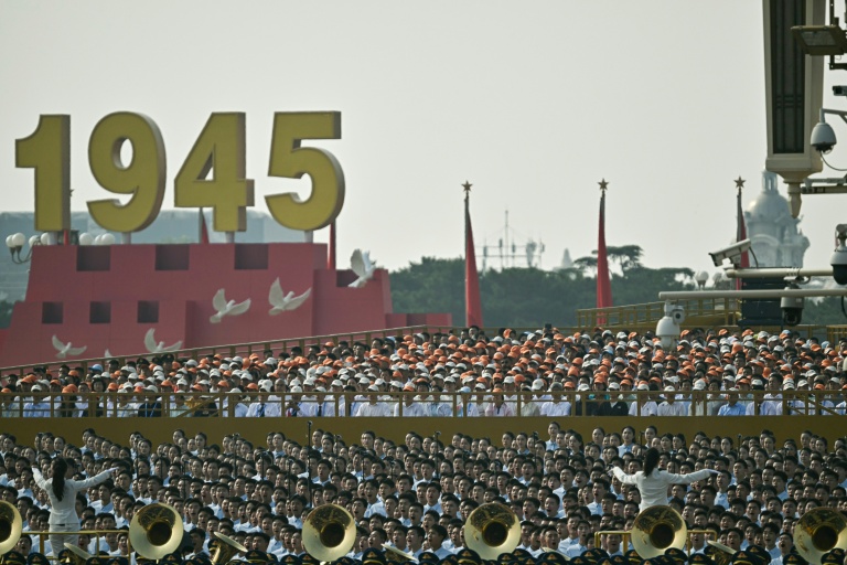 Des personnes chantent derrière une fanfare militaire avant un défilé militaire marquant le 80e anniversaire de la victoire sur le Japon et la fin de la Seconde Guerre mondiale, sur la place Tiananmen de Pékin le 3 septembre 2025