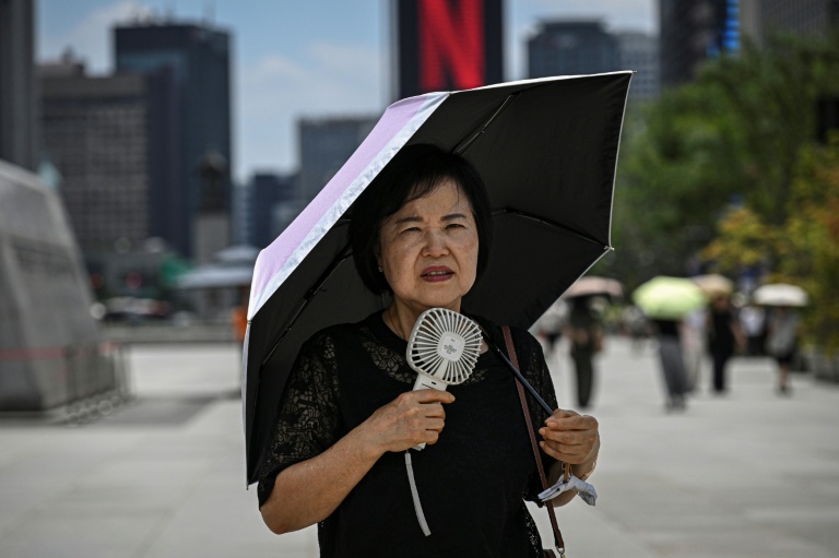 Une femme sous un parapluie avec un ventilateur portatif, le 12 juillet 2026 à Séoul 