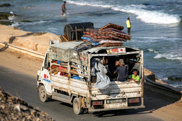 Des déplacés palestiniens fuyant le nord de la bande de Gza en direction du sud du terrtoire roulent à bord d'un camion chargé d'effets personnels sur la route côtière du camp de Nousseirat (centre), le 30 août 2025