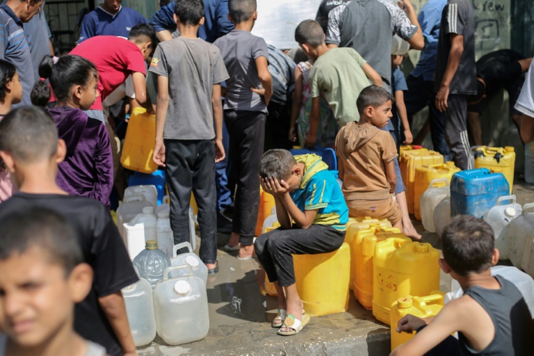 Des enfants palestiniens sont assis sur leurs conteneurs en attendant de les remplir à un point de distribution à Nousseirat, dans la bande de Gaza, le 4 septembre 2025