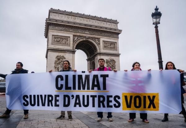 Des militants tiennent une banderole "Climat, écoutez les autres voix" lors d'une action de Greenpeace devant l'Arc de Triomphe à Paris, le 12 décembre 2025, à l'occasion du 10e anniversaire de la signature des accords de Paris sur le climat