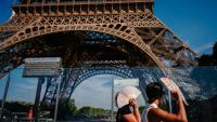 Des touristes se protègent du soleil avec des éventails en passant devant la tour Eiffel, fermée plus tôt en raison de la canicule, le 11 juillet 2026 à Paris