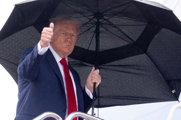 Le président américain Donald Trump tient un parapluie et lève le pouce alors qu'il monte à bord d'Air Force One avant son départ de la base aérienne d'Andrews, près de Washington, le 12 octobre 2025