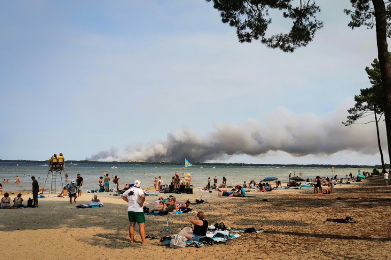 Des vacanciers sont assis sur la plage de Biscarrosse (sud-ouest), tandis qu'un épais nuage de fumée provoqué par un incendie s'élève dans le ciel, le 23 juillet 2026
