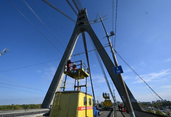Des techniciens réparent une ligne électrique de trolleybus à proximité des dégâts constatés sur un pilier du pont, à la suite d’une attaque de drone contre le pont du Nord à Kiev, le 3 octobre 2026