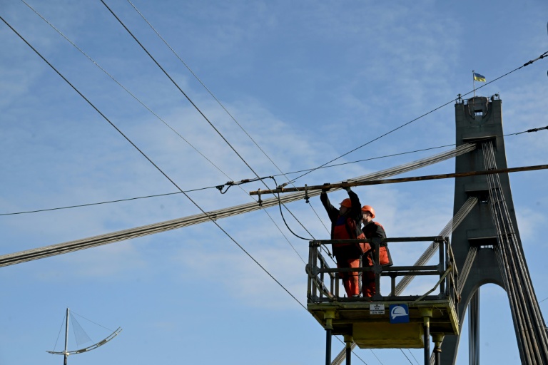 Des techniciens réparent une ligne électrique de trolleybus endommagée à la suite d'une attaque de drone contre le pont du Nord à Kiev, le 3 octobre 2026