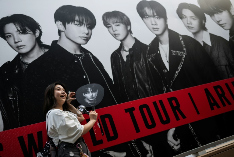 Une fan du groupe sud-coréen de K-pop BTS pose devant une affiche du groupe le 17 avril 2026 à Tokyo