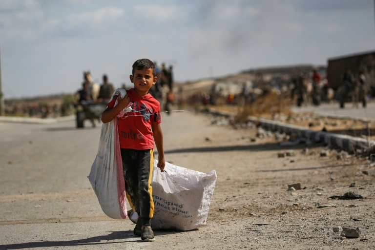 Un garçon palestinien porte un sac et traîne un autre derrière lui alors qu'il revient d'un point de distribution alimentaire dans le centre de la bande de Gaza, le 5 octobre 2025