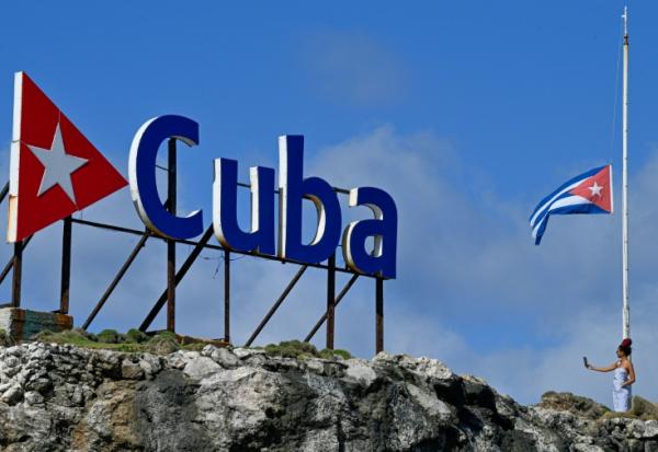 Une touriste prend un selfie alors qu’elle se tient à côté d’un drapeau national cubain en berne à La Havane, le 5 janvier 2026