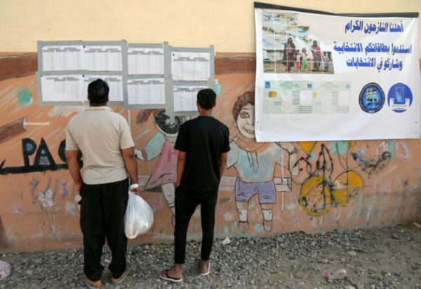 Des Irakiens déplacés consultent les listes nominatives affichées à l'extérieur d'un bureau de vote, à l'arrivée pour voter avant les élections législatives du 11 novembre, dans un camp du nord de l'Irak, le 9 novembre 2025