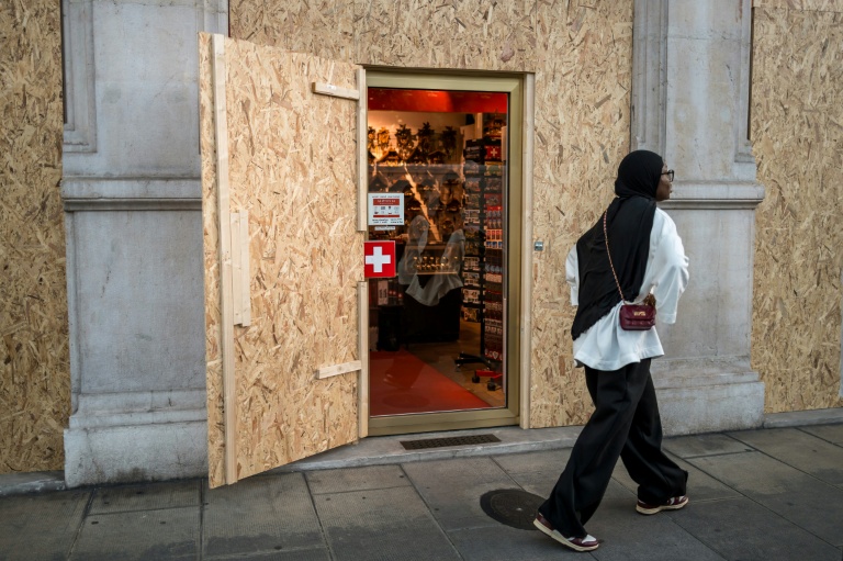 Une touriste passe devant un magasin de souvenir protégé par des panneaux de contreplaqué, le 12 juin 2026 à Genève, en Suisse, avant les manifestations anti-G7 en marge du sommet à Evian