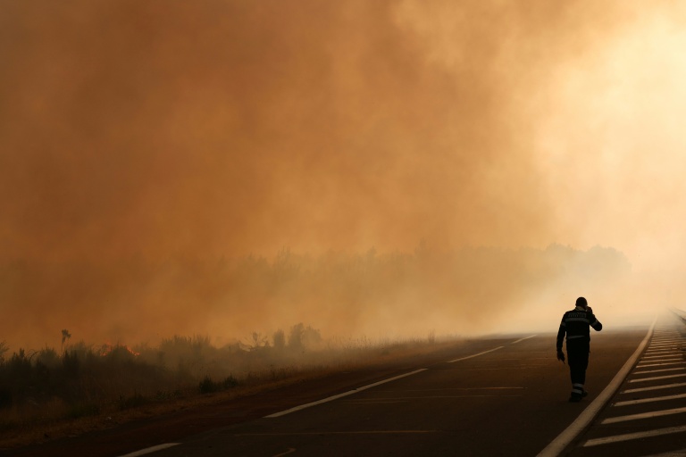 Un pompier marche sur une route en bordure d'une zone en feu à Ares, le 26 juillet 2026, alors qu'un incendie ravage la forêt au nord du bassin d'Arcachon en Gironde depuis le 22 juillet